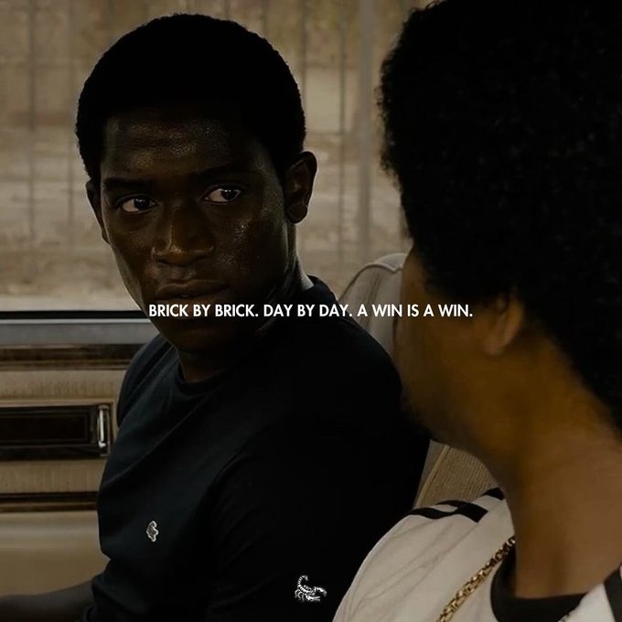 The image features two men sitting next to each other with one of them reading a quote from another man. The quote reads "Brick by brick, day by day, A win is a win". This quote seems to be related to the movie they are watching or discussing.