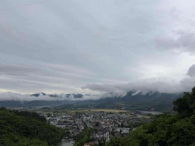 A panoramic view of a misty mountain valley with a small town nestled below, shrouded in low-hanging clouds and overcast skies. The dreamy, hazy atmosphere perfectly mirrors the surreal feeling of the poster's nightmare about waking up with only 300 days left until the gaokao, as if reality itself is as foggy and disorienting as a half-remembered dream.