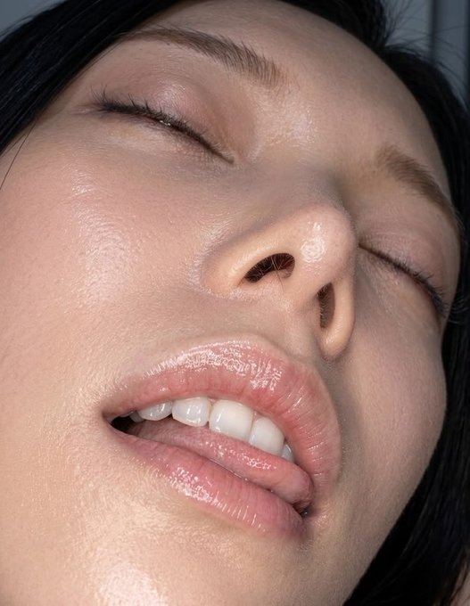 A close-up of a person's face with closed eyes, glossy lips slightly parted, and dewy skin—no text or branding visible in the image.