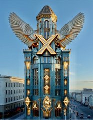 An ornate building featuring a large golden 'X' with wings design on its facade, with a clock tower visible.