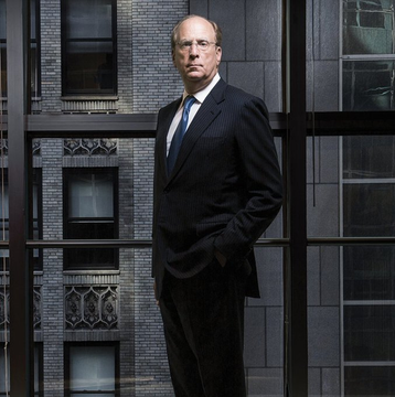A man in a dark suit stands confidently before a window reflecting a brick building, complementing the accompanying post about BlackRock CEO Larry Fink's bullish Bitcoin prediction.