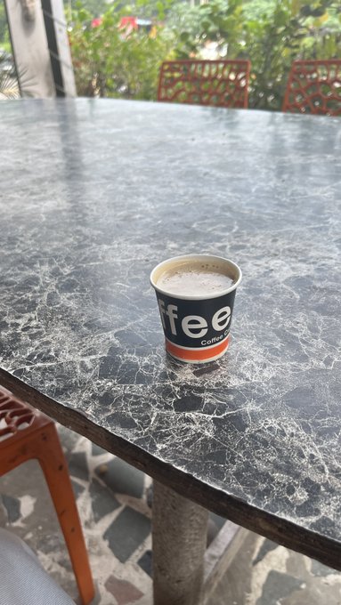 A small paper cup labeled 'fee Coffee House' containing a beverage, sitting on a black marble-patterned table.