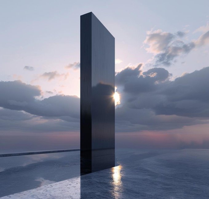 A tall, dark rectangular monolith stands vertically in a vast, flat landscape, with the sun setting behind it through scattered clouds, casting reflections on the wet surface below.