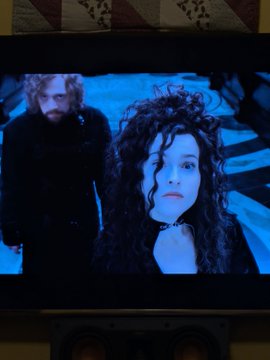 A photograph of a television screen displaying a scene with two characters bathed in blue light, one with long curly dark hair and the other with a beard in the background.