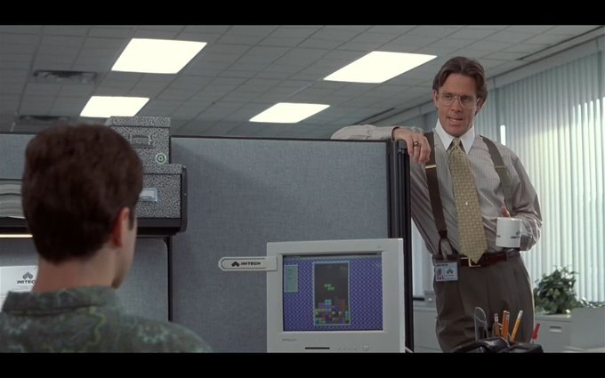 A scene from the movie Office Space showing the character Milton (Stephen Root) standing in a cubicle holding a mug.