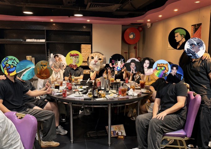 A group of people gather around a large round table in a dimly lit restaurant, their faces obscured by various colorful stickers and images including cats, anime characters, and memes, with drinks and food spread across the table as they enjoy a lively dinner gathering.