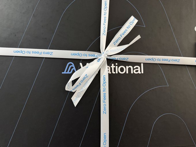 A black package wrapped with white ribbons printed with "Zero Fees to Open" surrounds the Variational logo, arriving as a gift package from the Variational team as mentioned in the post.