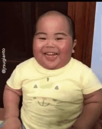 A smiling baby wearing a yellow shirt with a simple face design, with the watermark '@jrsugianto' visible.