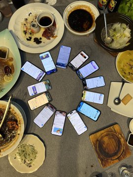 A group of friends gathered around a dining table, with their smartphones arranged in a circle displaying social media or chat conversations, alongside various dishes and drinks, capturing the social connections made at Bored Ape Yacht Club's "Ape Into Asia" Shanghai event.