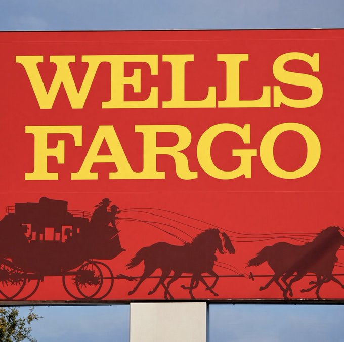 A large red and yellow Wells Fargo sign featuring the iconic stagecoach logo illustrates the post about the banking giant exploring a crypto liquidity partnership with Kraken parent company Payward. The image visually anchors the story of traditional Wall Street firms increasingly engaging with the cryptocurrency industry.