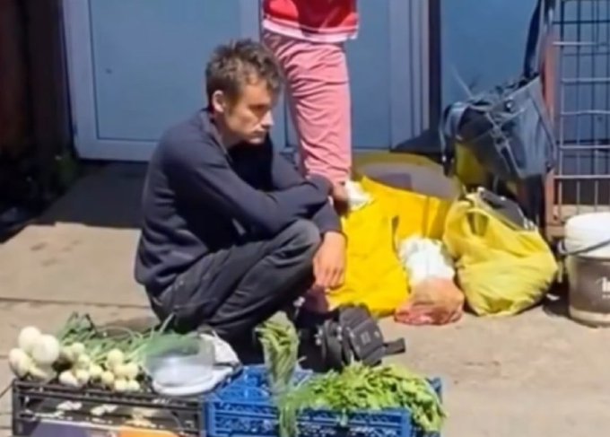 The image shows a man kneeling next to a blue crate filled with vegetables, including onions and potatoes. He appears to be selling these items on the street. The photo also includes a person standing nearby who seems interested in the produce being sold by Vitalik. A handbag can be seen close to the man selling vegetables, suggesting that he might have purchased it from him as well.

The post about Vitalik's vegetable stand is titled "ETH is down so bad Vitalik is now selling veggies on the street". This implies that the market conditions are unfavorable for Vitalik and his vegetable stand, possibly due to a decrease in demand or supply of fresh produce.