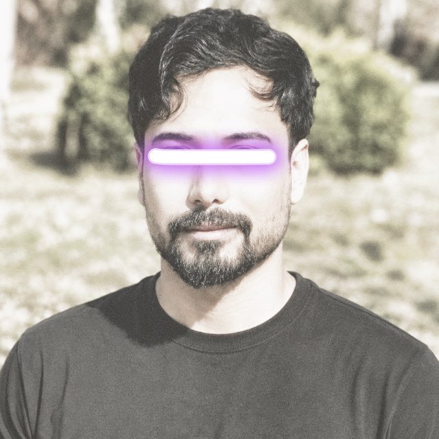 A man with dark hair and a beard wearing a dark t-shirt, with a bright purple glowing bar covering his eyes, set against a blurred outdoor background.