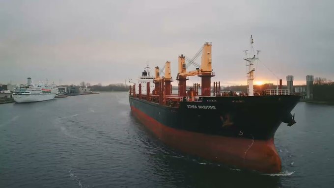 A large cargo ship labeled "ETHRA MARITIME" sails through a waterway at sunset, with its distinctive red and black hull and multiple cranes visible against the dusky sky. The image illustrates EthraShip's real-world maritime asset backing, reinforcing the post's point about the project's tangible shipping operations rather than just token-based promises.