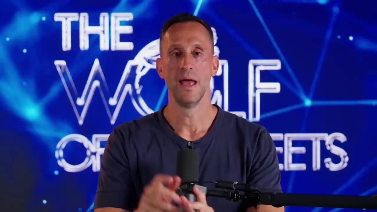 The image features a man wearing a blue shirt, standing behind a microphone with his hands up as if he's speaking into it. The background of the image has a blue color scheme, which complements the man's attire. The text "THE WOLF OF WEETS" is displayed in white letters above and to the right of the man, while "bitcoin" is written in black letters below him. This suggests that the image might be related to a discussion or presentation about Bitcoin or cryptocurrency.