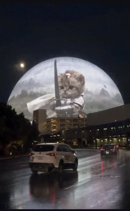 A surreal digital illustration showing a giant sad kitten holding a sword in front of a full moon, looming over a city street with cars at night.