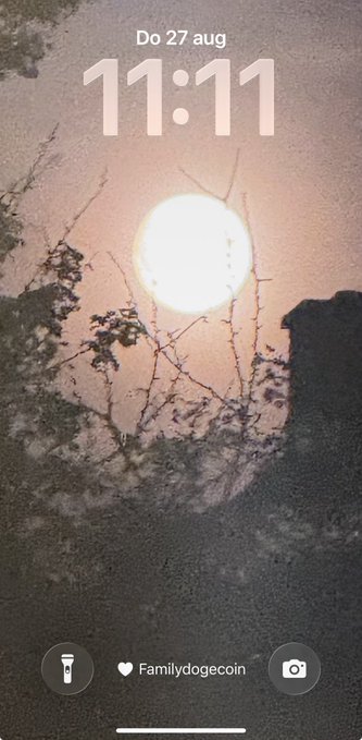A phone lock screen showing the time 11:11 on Do 27 aug (Thursday, August 27), with lock screen wallpaper depicting a sunset/sunrise scene reflected through wet glass or a window with the widget 'Familydogecoin'.