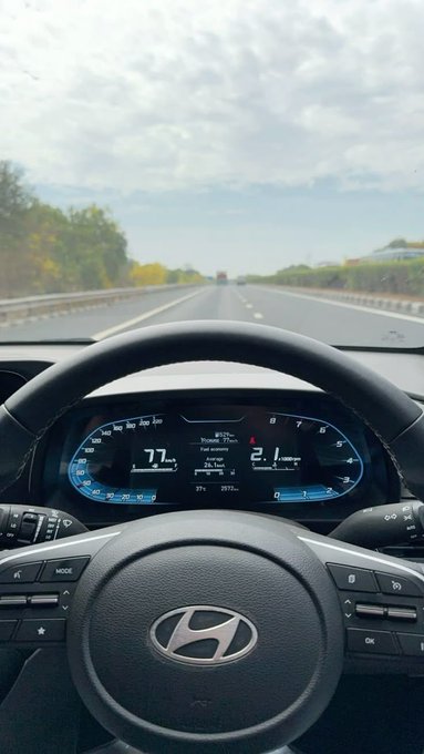A view from the driver's seat of a Hyundai vehicle driving on a highway, with the digital dashboard showing a speed of 77 mph.