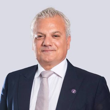 A professional headshot of a smiling older man with grey hair, wearing a dark blue suit, white shirt, and light pink tie.