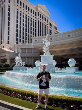 A person poses in front of the Caesars Palace hotel and its ornate fountain feature.