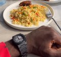 A wrist wearing a watch rests on a table next to a plate of food with a fork.