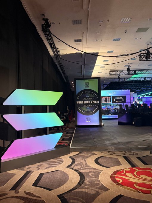 A casino conference floor features a "World Series of Poker" promotional display alongside colorful, arrow-shaped light panels, evoking the high-stakes environment where Solana's "Breakpoint" event is being held.