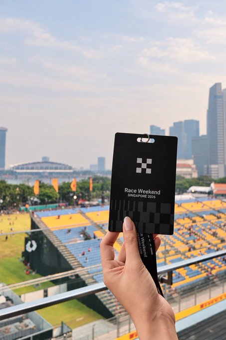 A hand holding a black 'Race Weekend Singapore 2025' event pass/lanyard with a checkered flag logo, overlooking a race circuit with stadium seating and city skyline.