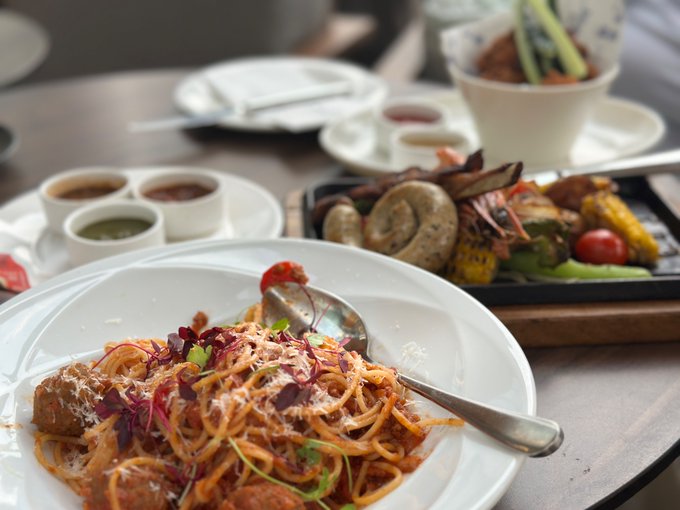 A plate of spaghetti with meatballs and herbs sits in the foreground, accompanied by a tray of grilled meats and vegetables, along with small dipping sauces on the side.

Note: The image shows a meal of pasta and grilled dishes, which doesn't appear to relate to the accompanying post about being recognized in a Marriott elevator while wearing a Huobi T-shirt.
