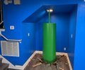 A green model of a rocket stands vertically on a test stand in a blue room.