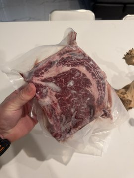A hand holds up a vacuum-sealed bone-in ribeye roast, with an accompanying post inviting guesses on the dollar amount paid for the prime cut, offering 2100 sats to the closest estimate.