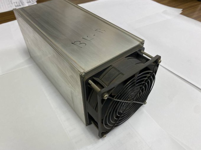 A metallic industrial device, likely an ASIC miner, labeled 'BV-8', with a cooling fan visible on one end, sitting on white paper.