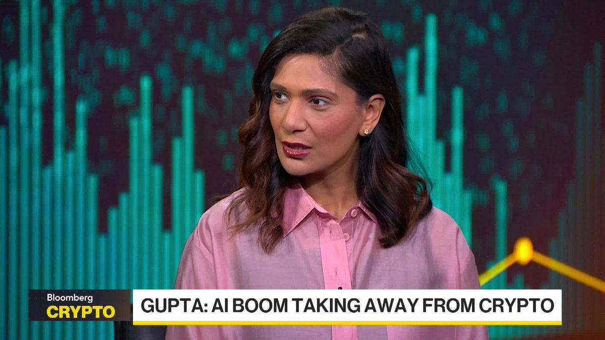 Bloomberg Crypto anchor interviews a guest on set about the recent AI boom potentially diverting attention and capital away from the crypto sector, as shown by the on-screen graphic "GUPTA: AI BOOM TAKING AWAY FROM CRYPTO." The interview appears to discuss whether institutional money from AI-related deals may rotate back into digital assets.