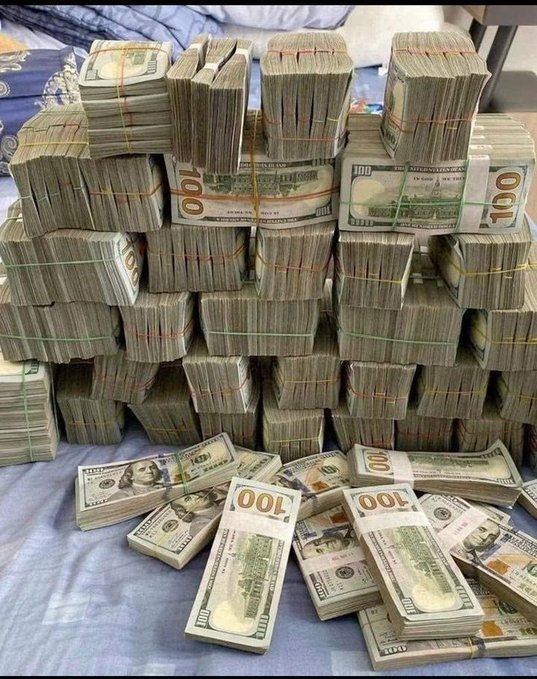 A photograph showing numerous banded stacks of U.S. one-hundred-dollar bills piled together on a blue fabric surface.