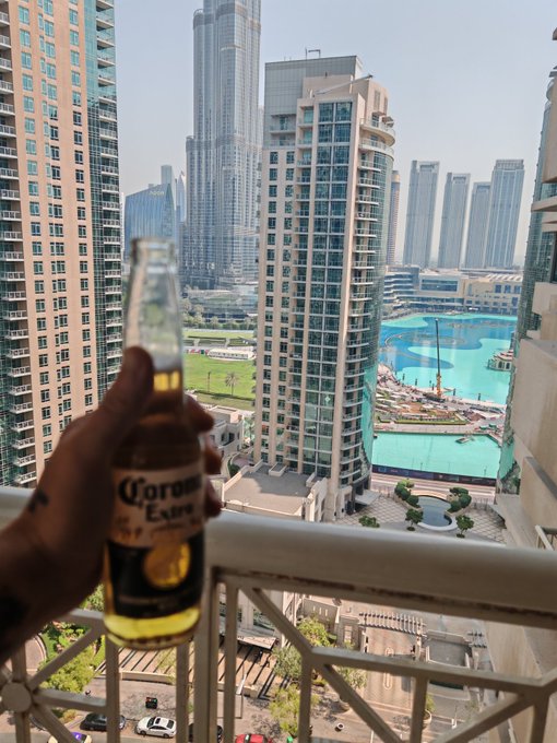A hand holds a Corona Extra beer bottle on a balcony overlooking a cityscape of high-rise buildings and a turquoise pool, perfectly capturing the relaxed "spicy Tuesday" vibe the poster wishes their Web3 community.