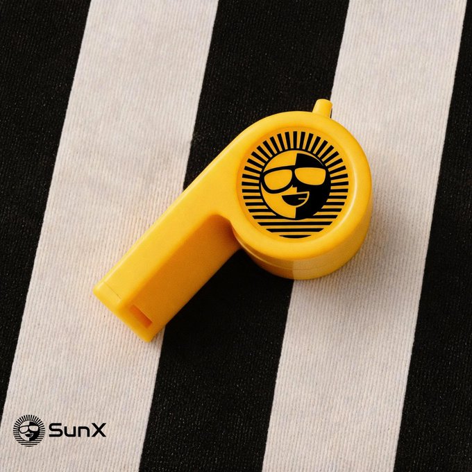 A yellow SunX whistle featuring the logo of a smiling face wearing sunglasses with sun rays, photographed on a black and white striped background with the SunX watermark.