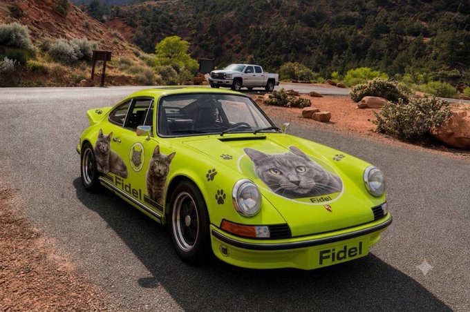 A bright yellow-green vintage Porsche-style sports car decorated with cat graphics and the name 'Fidel' is parked in a desert landscape with a pickup truck in the background.