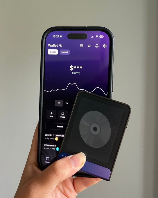 A hand holds a hardware wallet against a smartphone displaying a crypto portfolio with Bitcoin and Ethereum balances, visually reinforcing the post's message that true ownership of digital assets requires a physical device rather than reliance on third-party servers.