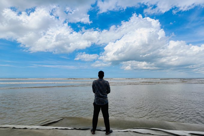 A person silhouetted from behind, standing on a platform and looking out at a vast, cloudy ocean horizon.