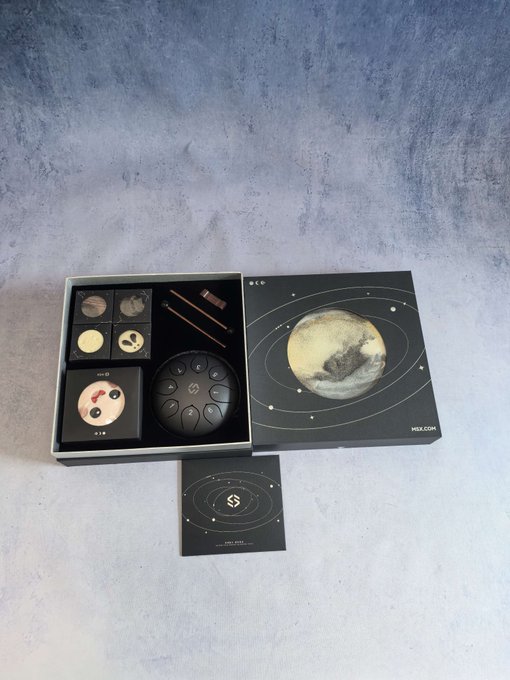 An open product box featuring a moon-themed design with various small items including a round black device, a lipstick, and other accessories arranged inside.
