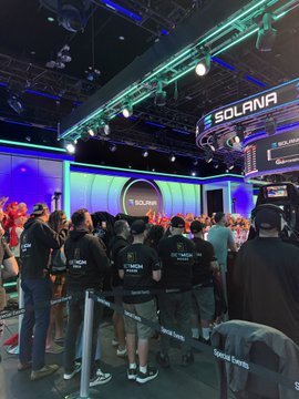 A crowded indoor event space with a 'SOLANA' sign displayed prominently on a digital screen and above a booth, where attendees are gathered.