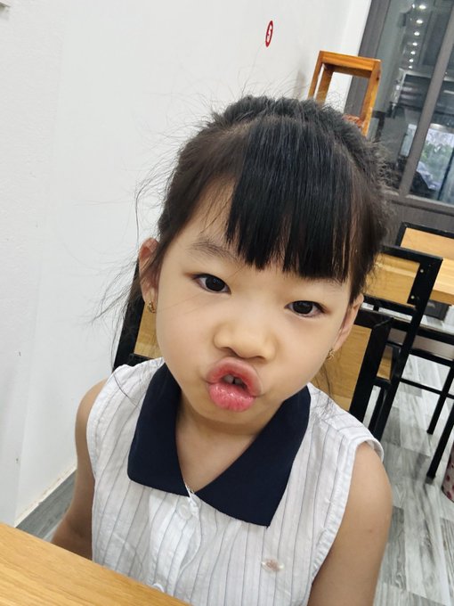 A young girl with bangs in a white and navy top makes a playful pouting face indoors.