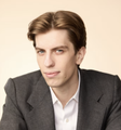 A young man in a dark blazer gazes intensely at the camera, reflecting the serious, urgent tone of the stream caption referencing Leopold Aschenbrenner's apparent liquidation of top losers.