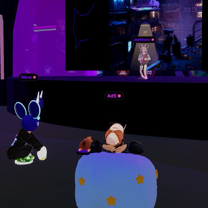 Avatars named 'iMew', 'Ad5', and 'JoeName' gather in a virtual reality space with a cyberpunk cityscape displayed on a screen.