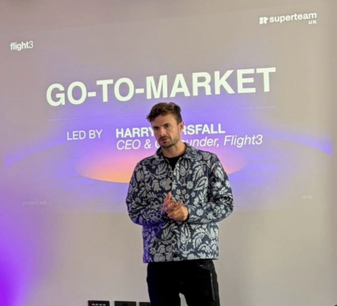 A man in a patterned shirt stands presenting in front of a screen displaying 'GO-TO-MARKET LED BY HARRY [GR]SFALL CEO & [F]ounder, Flight3' with logos for 'flight3' and 'superteam UK'.