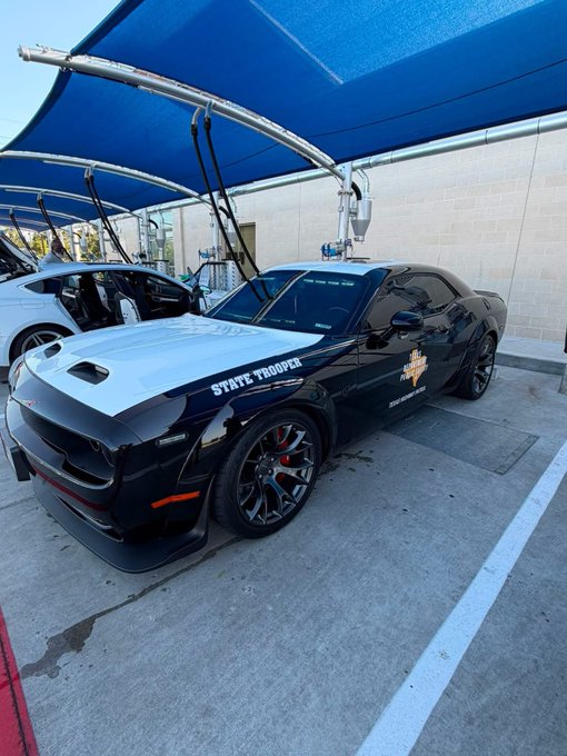 A sleek black and white Chevrolet Camaro "STATE TROOPER" police vehicle with red brake calipers and a gold star badge on the door is parked under a blue canopy, perfectly embodying the post's warning that "You're not going to outrun this one." The car's aggressive styling and performance wheels reinforce the threatening caption.