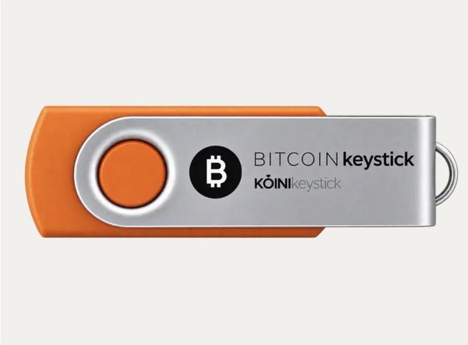 An orange and silver USB drive branded 'BITCOIN keystick' by KoinKeep, a hardware wallet designed for storing Bitcoin.