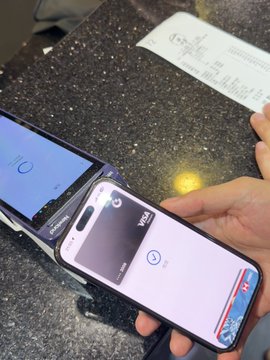 Two smartphones rest on a dark countertop; one shows a blue screen and the other displays a camera viewfinder app with 'PLAY' branding, with a receipt visible nearby.