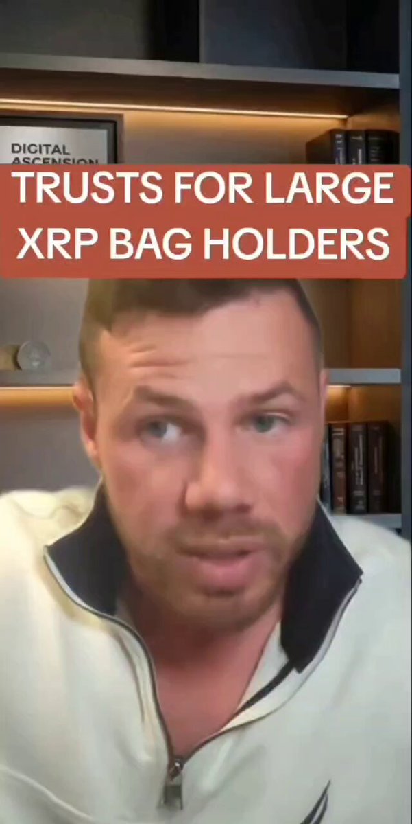 The image features a man wearing a white jacket, sitting at a desk with books around him. The text displayed on the image reads "Trusts for Large XRP Bag Holders", which suggests that the man might be discussing trusts or estate planning related to cryptocurrency and XRP specifically.