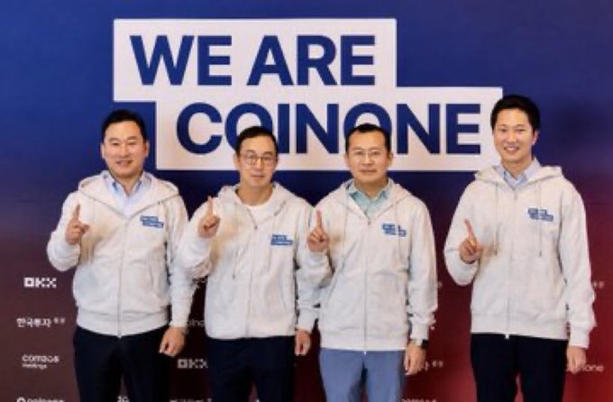 Four men pose in matching white hoodies in front of a "WE ARE COINONE" banner, with sponsor logos like OKX and Deutsche visible below, representing the Coinone exchange team following OKX Ventures' acquisition of a 20% stake.