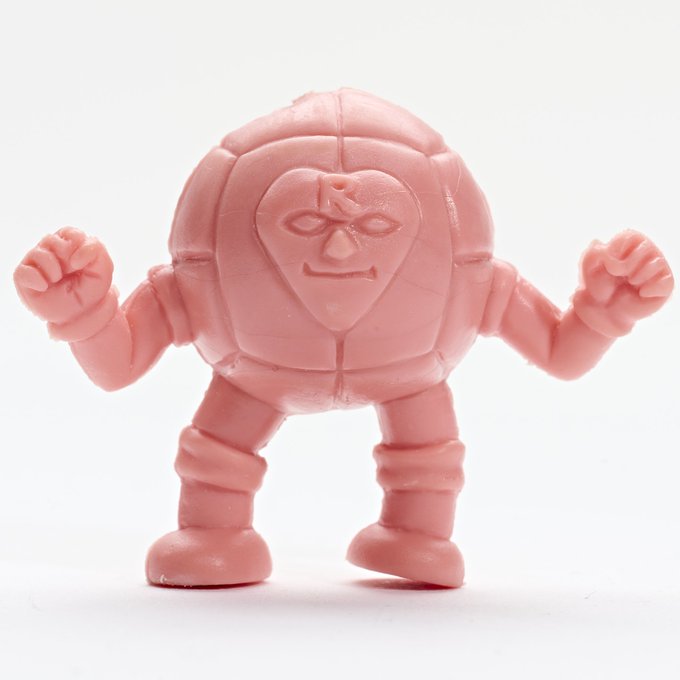 A small pink rubber figurine of a muscular cartoon character with clenched fists and an angry expression stands against a white background.