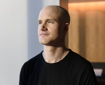 A bald man in a black t-shirt is photographed in profile, looking off to the side with a neutral expression in a softly lit interior setting.